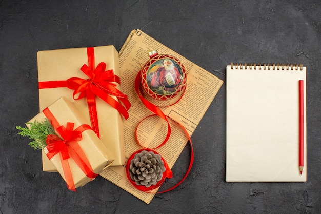 Vista superior de regalo de Navidad en cinta de papel marrón, juguete de árbol de Navidad en el periódico, un lápiz, un cuaderno sobre una superficie oscura