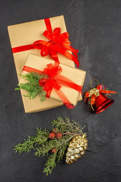 Vista superior de regalo de Navidad en papel marrón atado con adornos de árbol de Navidad de abeto de rama de cinta roja sobre fondo oscuro