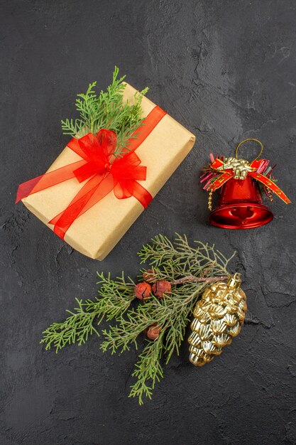 Vista superior de regalo de Navidad en papel marrón atado con adornos de árbol de Navidad de rama de abeto de cinta roja sobre superficie oscura