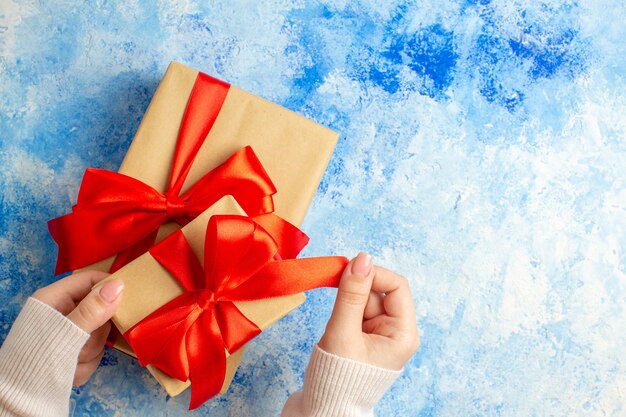 Vista superior de los regalos de Navidad atados con lazo rojo en la mano femenina en el espacio libre de la mesa azul