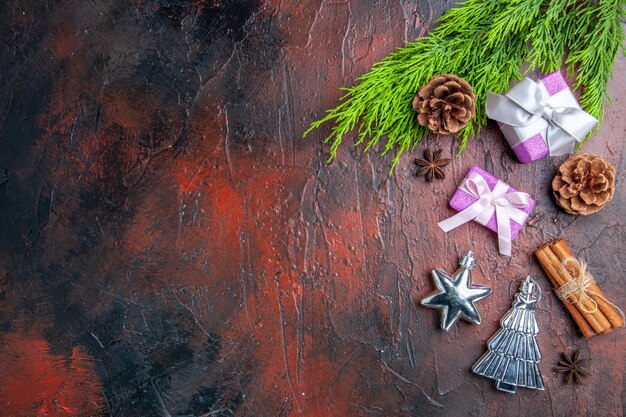 Vista superior de regalos de Navidad con caja rosa y cinta blanca rama de árbol anís canela juguetes de árbol de Navidad sobre fondo rojo oscuro