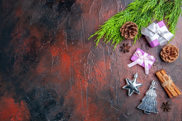 Vista superior de regalos de Navidad con caja rosa y cinta blanca rama de árbol anís canela juguetes de árbol de Navidad sobre fondo rojo oscuro