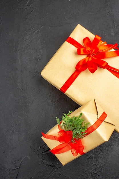Vista superior de regalos de Navidad grandes y pequeños en papel marrón atado con abeto de rama de cinta roja sobre superficie oscura
