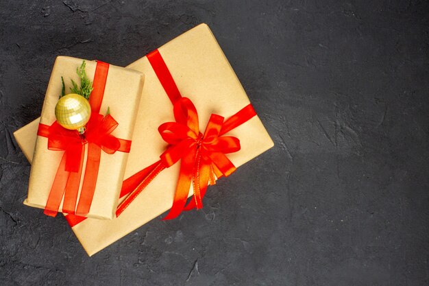 Vista superior de regalos de Navidad grandes y pequeños en papel marrón atado con cinta roja sobre una superficie oscura