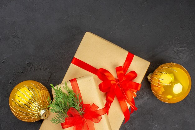 Vista superior de regalos de Navidad grandes y pequeños en papel marrón atados con bolas de cinta roja sobre una superficie oscura