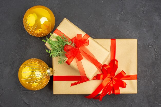 Vista superior de regalos de Navidad grandes y pequeños en papel marrón atados con bolas de Navidad de abeto de rama de cinta roja sobre superficie oscura
