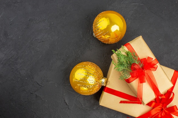 Vista superior de regalos de Navidad grandes y pequeños en papel marrón atados con bolas de Navidad de cinta roja sobre una superficie oscura