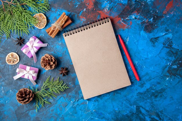 Vista superior regalos de navidad ramas de abeto conos anises cuaderno lápiz sobre superficie azul