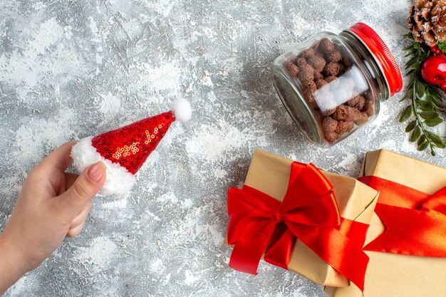 Vista superior de regalos de Navidad sombrero de santa en cereal de mano femenina en tarro en mesa gris