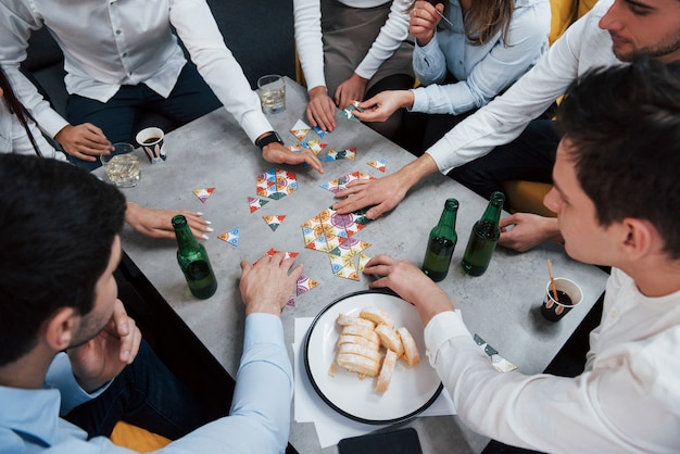 Vista superior. Relajante con juego. Celebrando el trato exitoso. Jóvenes oficinistas sentados cerca de la mesa con alcohol