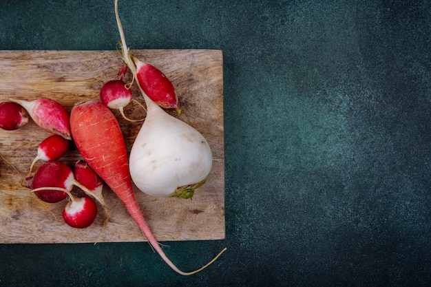 Foto gratuita vista superior de remolachas vegetales orgánicos de raíz blanca y rosada en una tabla de cocina de madera con rábanos sobre una superficie verde con espacio de copia