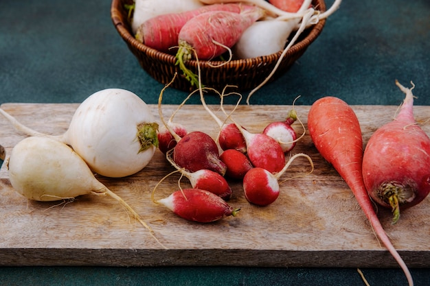 Vista superior de remolachas vegetales de raíz roja rosada y blanca fresca en una tabla de cocina de madera con rábanos sobre una superficie verde