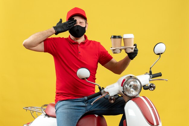 Vista superior del repartidor emocional nervioso con uniforme y guantes de sombrero en máscara médica sentado en scooter mostrando pedidos