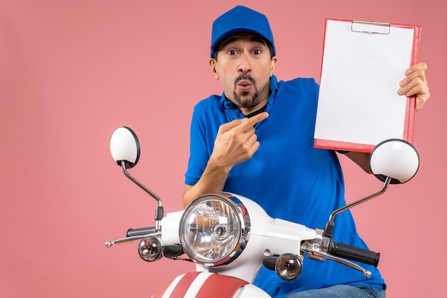 Foto gratuita vista superior del repartidor masculino sorprendido con sombrero sentado en scooter sosteniendo documento