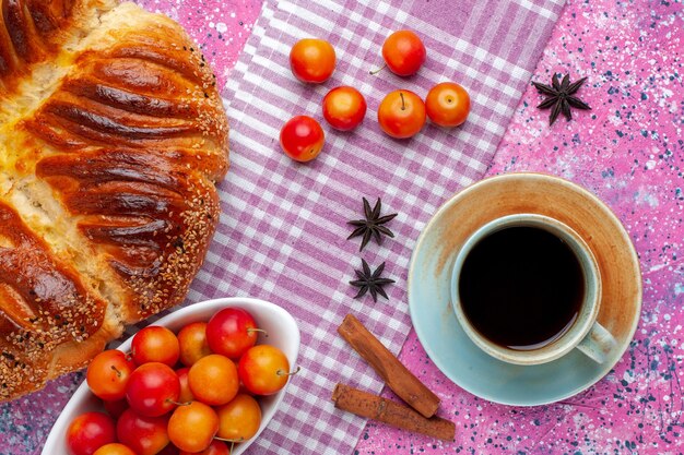 Vista superior de repostería al horno con ciruelas canela y taza de té en el escritorio rosa.