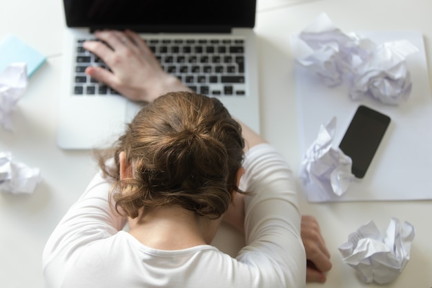 Vista superior retrato de mujer acostada en escritorio cerca de la computadora portátil