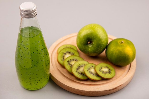 Vista superior de rodajas de kiwi fresco picado en una tabla de cocina de madera con manzana verde y mandarina con jugo de kiwi fresco en una botella de vidrio