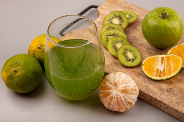 Vista superior de rodajas de kiwi picado saludables con mandarina y manzana en una tabla de cocina de madera con jugo de fruta fresca