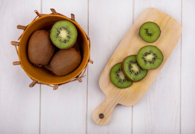 Foto gratuita vista superior de rodajas de kiwi en la tabla de cortar con todo en la canasta en la pared blanca