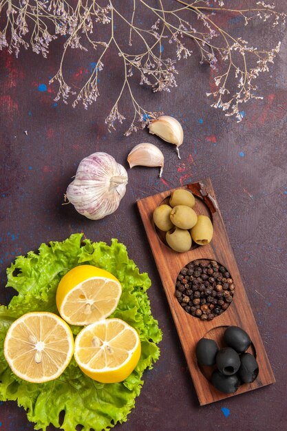 Vista superior de rodajas de limón con aceitunas y ensalada verde sobre negro