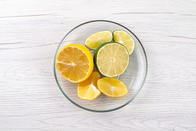 Una vista superior en rodajas de limón agrio jugoso dentro de un tazón de vidrio sobre un escritorio blanco, jugo de fruta