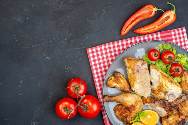 Vista superior rodajas de limón pollo al horno en placa tomates pimientos picantes en negro