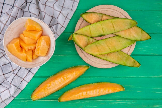 Vista superior de rodajas maduras picadas de melones en un tazón sobre mantel controlado sobre superficie verde