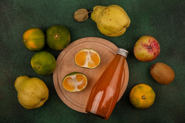 Vista superior de rodajas de mandarina en un soporte con peras, manzana, kiwi y una botella de jugo.