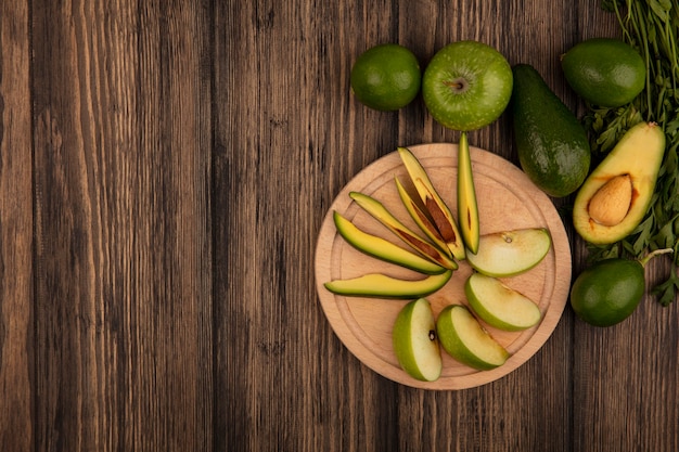 Vista superior de rodajas de manzana fresca en una tabla de cocina de madera con rodajas de aguacate con manzanas enteras, limones de aguacate y perejil aislado en una superficie de madera con espacio de copia