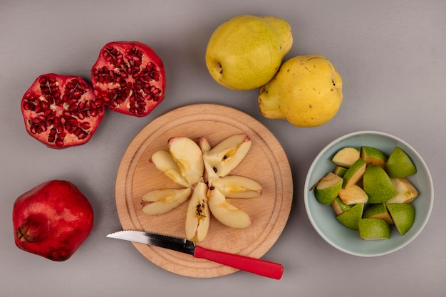 Vista superior de rodajas de manzana picada fresca sobre una tabla de cocina de madera con cuchillo con granadas y membrillos aislado