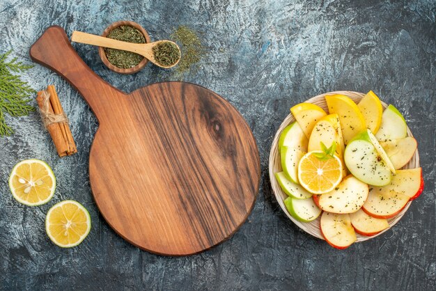 Vista superior de rodajas de manzana roja verde amarillo fresca en un plato blanco con limón sobre una tabla de cortar de madera limones canela sobre fondo gris