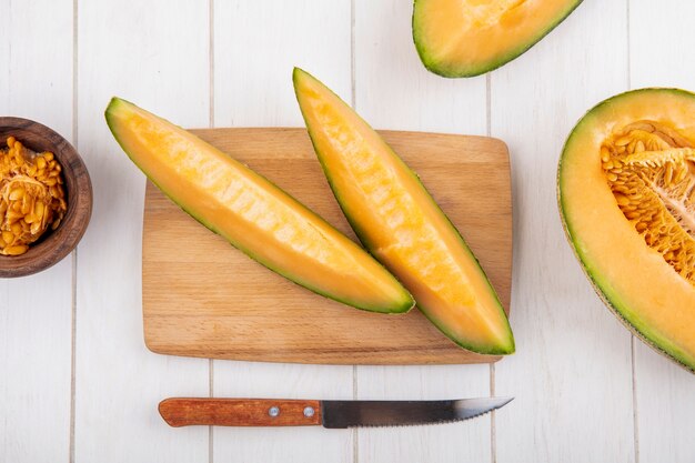 Vista superior de rodajas de melón cantalupo fresco y delicioso en tablero de cocina de madera con cuchillo en madera blanca