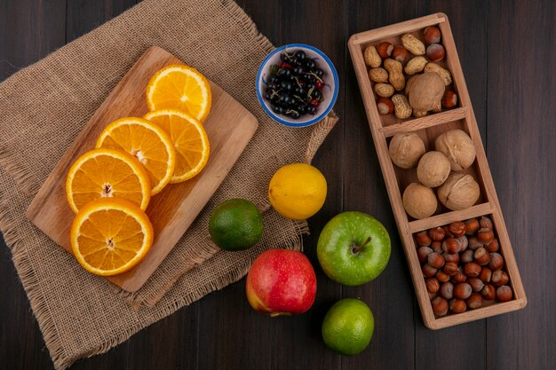 Vista superior de rodajas de naranja sobre una placa en una servilleta beige con manzanas, grosellas negras de limón y nueces sobre una superficie de madera