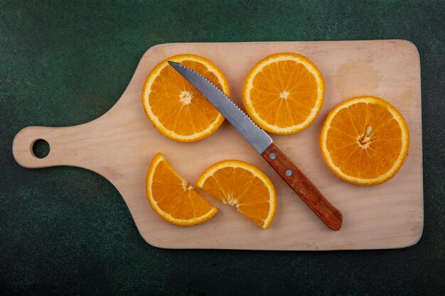 Vista superior de rodajas de naranja en la tabla de cortar con un cuchillo sobre fondo verde