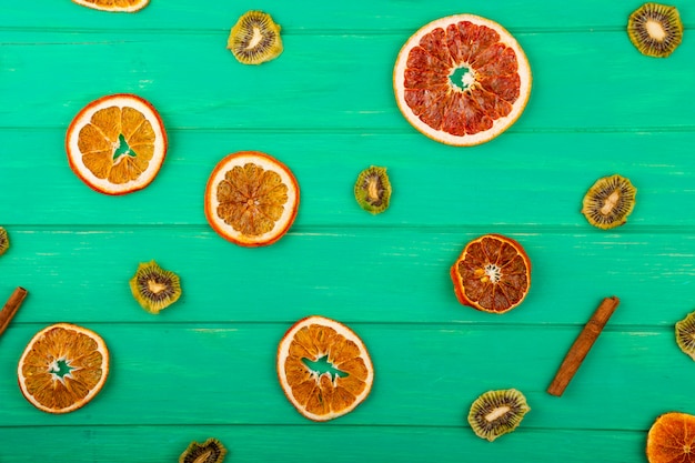 Vista superior de rodajas de naranja y toronja secas con palos secos de kiwi y canela sobre fondo de madera verde