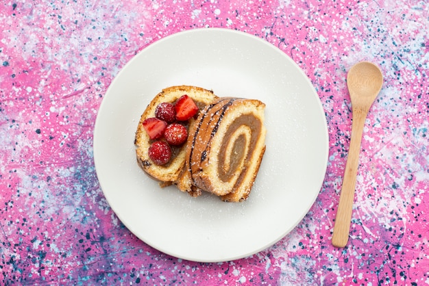 Foto gratuita vista superior rodajas de pastel de rollo dentro de un plato blanco con rodajas de fresa en el escritorio púrpura pastel galleta azúcar dulce