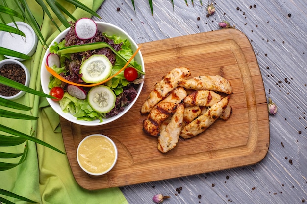 Vista superior rodajas de pechuga de pollo a la plancha con ensalada de verduras y salsa en el tablero