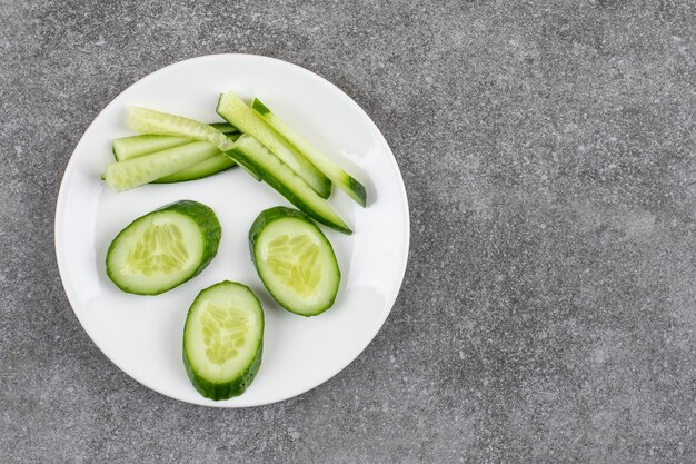 Vista superior de rodajas de pepino en rodajas y picadas en un plato blanco sobre una mesa gris.