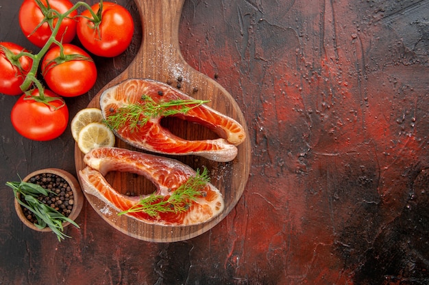 Foto gratuita vista superior de rodajas de pescado crudo con tomates rojos sobre fondo rojo oscuro