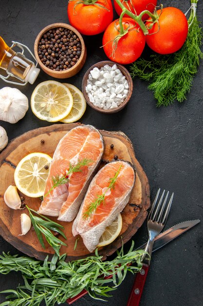 Vista superior de rodajas de pescado fresco con condimentos y rodajas de limón en la mesa oscura