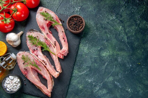 Vista superior de rodajas de pescado fresco con pimiento y tomates sobre fondo azul oscuro