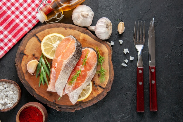 Vista superior de las rodajas de pescado fresco con rodajas de limón, ajo y condimentos en la mesa oscura