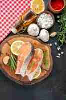 Foto gratuita vista superior de las rodajas de pescado fresco con rodajas de limón, ajo y condimentos en la mesa oscura