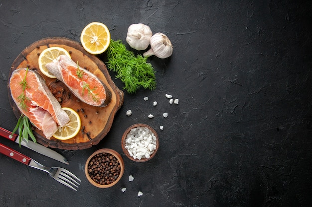 Vista superior de rodajas de pescado fresco con rodajas de limón y ajo en la mesa oscura