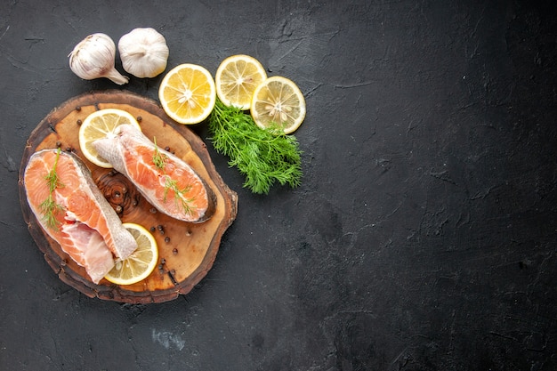 Vista superior de las rodajas de pescado fresco con rodajas de limón en la mesa oscura