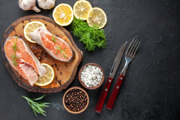 Vista superior de las rodajas de pescado fresco con rodajas de limón en la mesa oscura