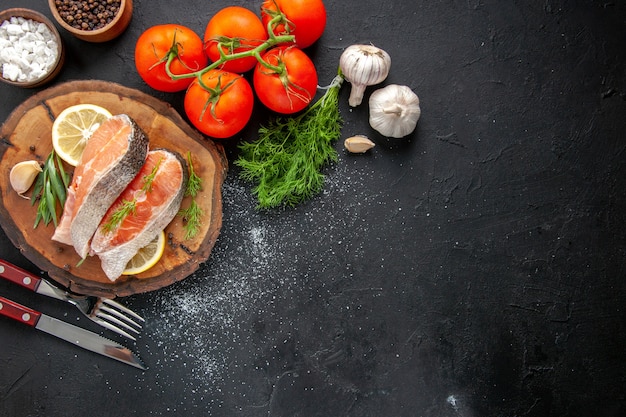 Vista superior de rodajas de pescado fresco con rodajas de limón y tomates en la mesa oscura