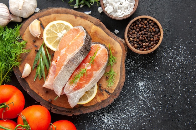 Vista superior de rodajas de pescado fresco con tomates y rodajas de limón en la mesa oscura