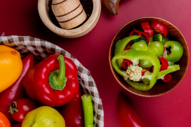 Vista superior de rodajas de pimiento en un tazón con verduras como tomate pimiento en una cesta con trituradora de ajo en la superficie del tablero