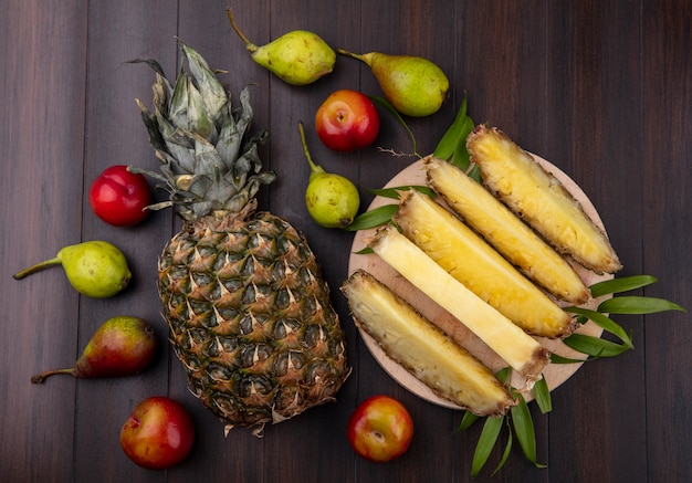 Vista superior de rodajas de piña en un plato con manzana entera y durazno sobre superficie de madera